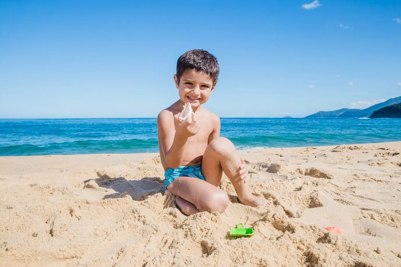 Fröhlicher kleiner Junge mit einer Muschel am Strand