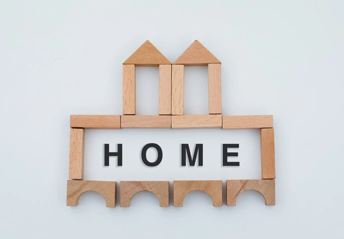 Flatlay eines Hauskonzepts mit einer unvollständigen Holzburg auf weißem Hintergrund.